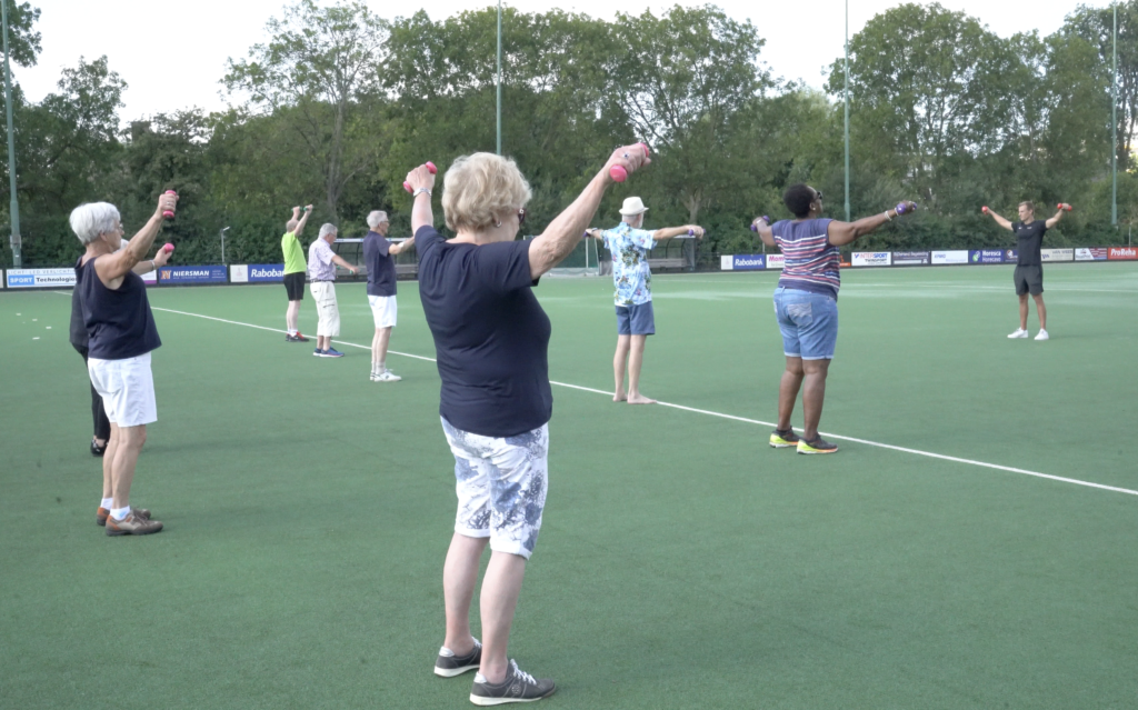 Ludios instructeur begeleidt een groep ouderen bij een laagdrempelige beweegactiviteit buiten op het sportveld